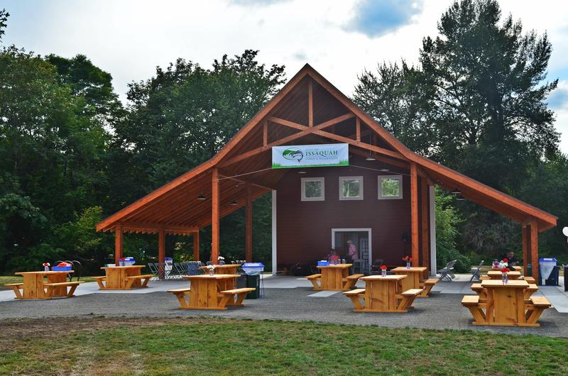 Wooden play structure with a roof at Confluence Park in Issaquah, with the creek behind it.