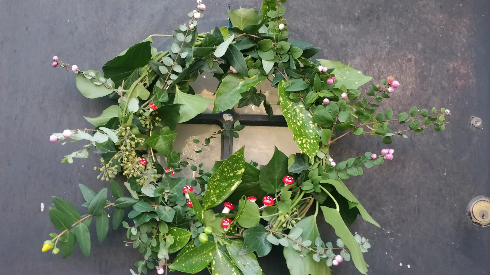 A green Christmas wreath with red berries on a dark door.
