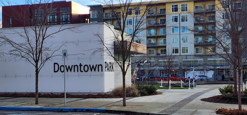 The lawn and path at Downtown Park in Redmond, with evergreens and carved house poles.