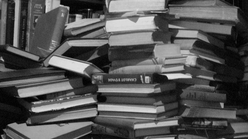 A stack of hardcover books on a wooden table.