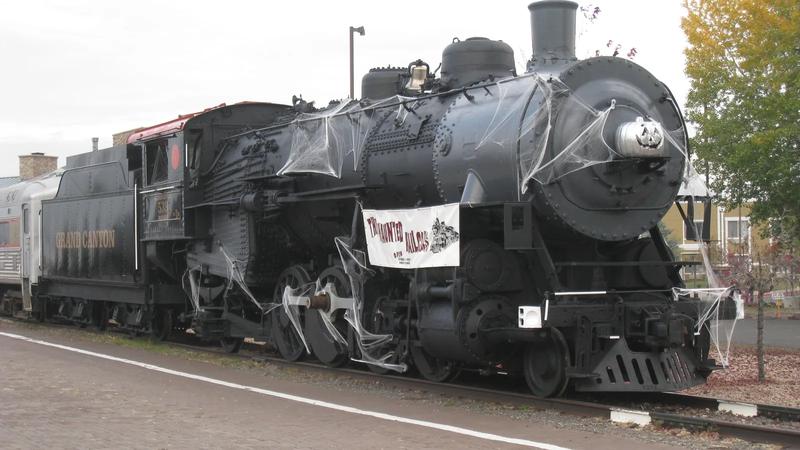 A black steam locomotive decorated for Halloween, with a ghost painted on the front.