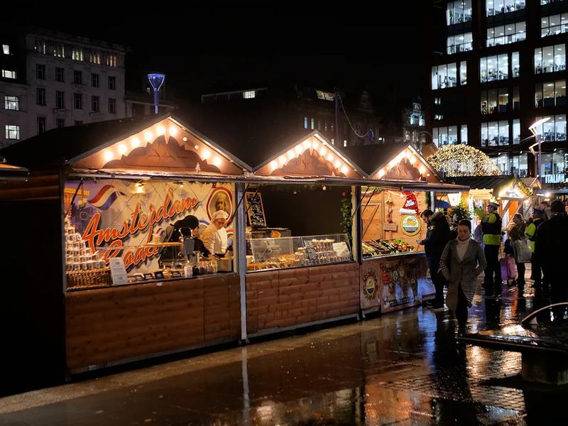 Wooden chalet stalls at a Christmas market, with red and green roofs.