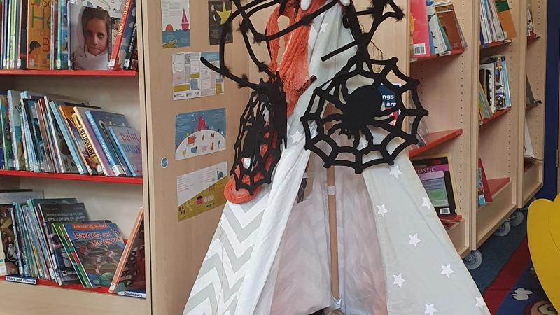 A library reading nook dressed for Halloween, with paper bats, a spiderweb, and a black cat.