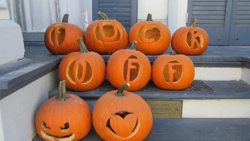 Pumpkins lined up along a sidewalk on a city street.